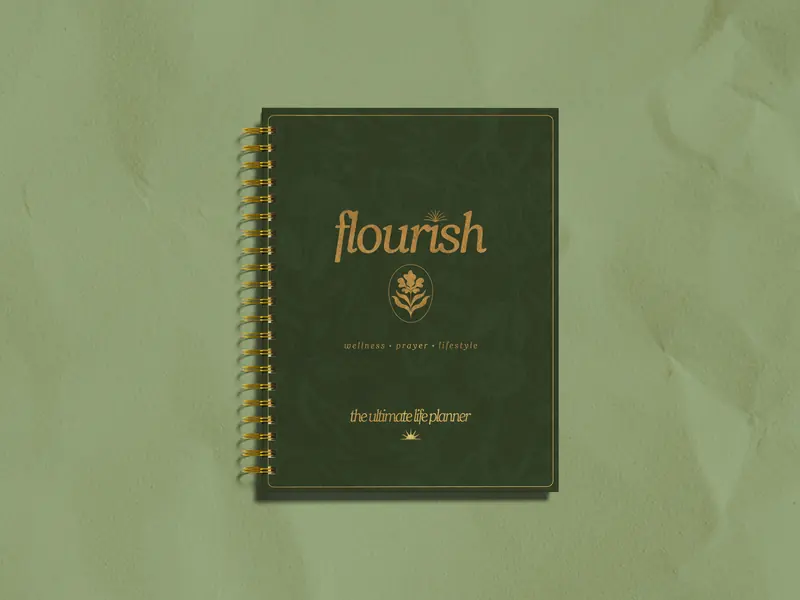The Flourish life planner by Michelle Johnson, deep green cover with gold lettering, on a sage background