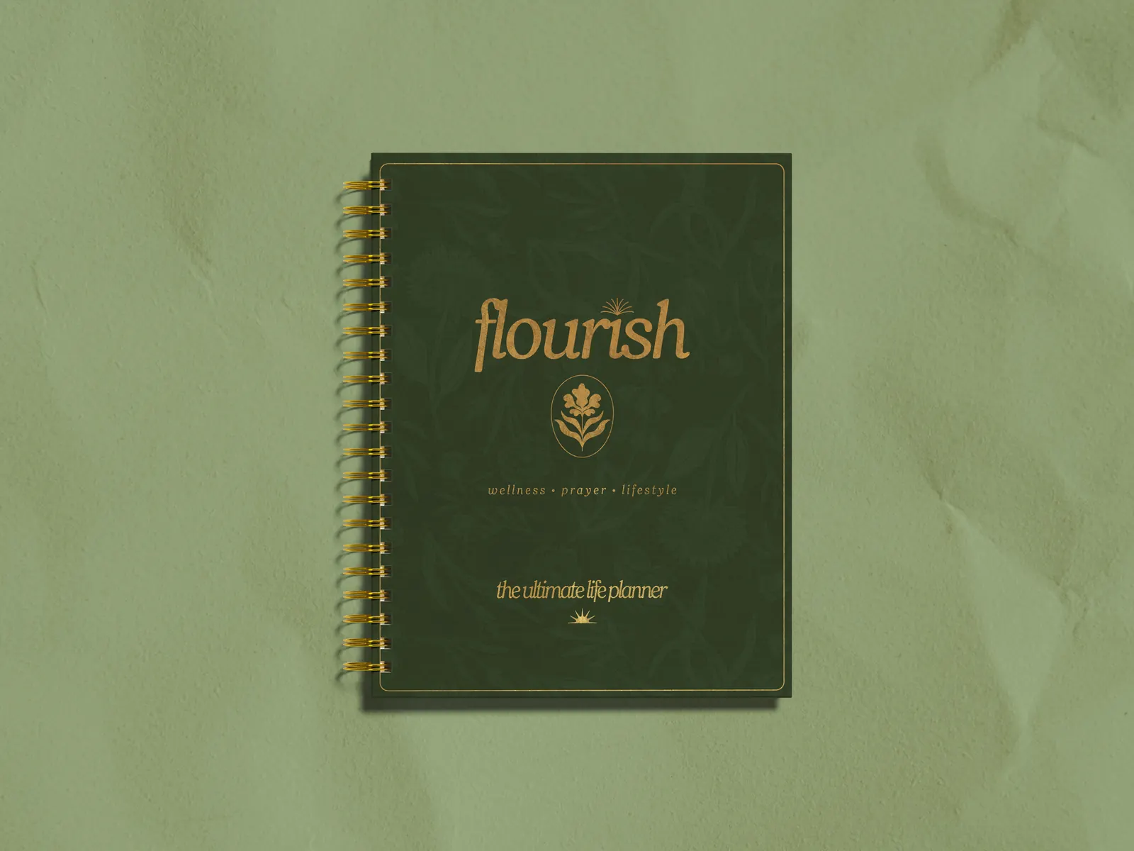 The Flourish life planner by Michelle Johnson, deep green cover with gold lettering, on a sage background