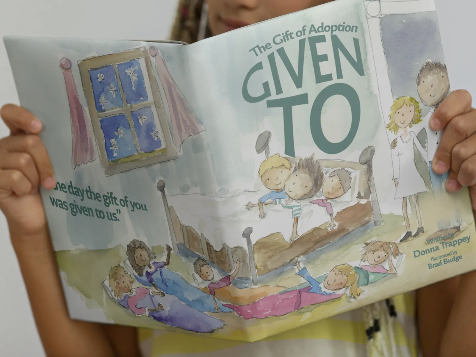 A child holding open the picture book Given To: The Gift of Adoption