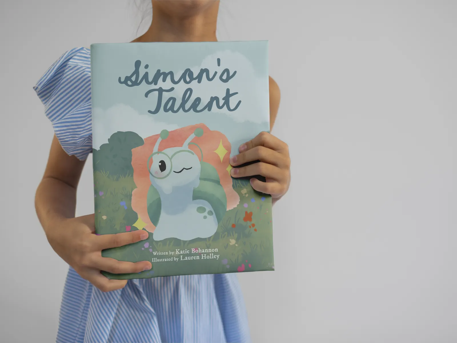 A child holding the hardback picture book Simon's Talent in front of her