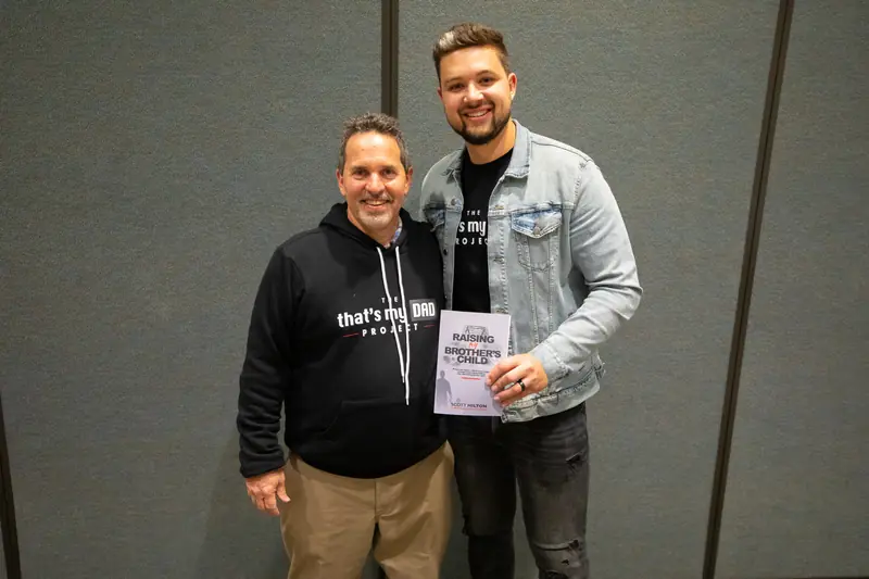 Colin Edwards and Scott Hilton holding a copy of Raising My Brother's Child