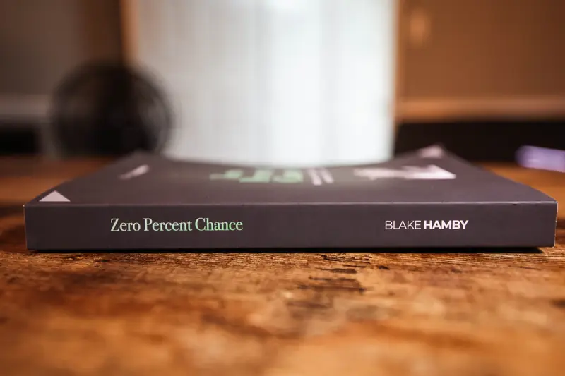 The spine of Zero Percent Chance on a wooden table under a coffee mug